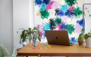 macbook on a modern wood work table in front of a modern art canvas, ways to build your business